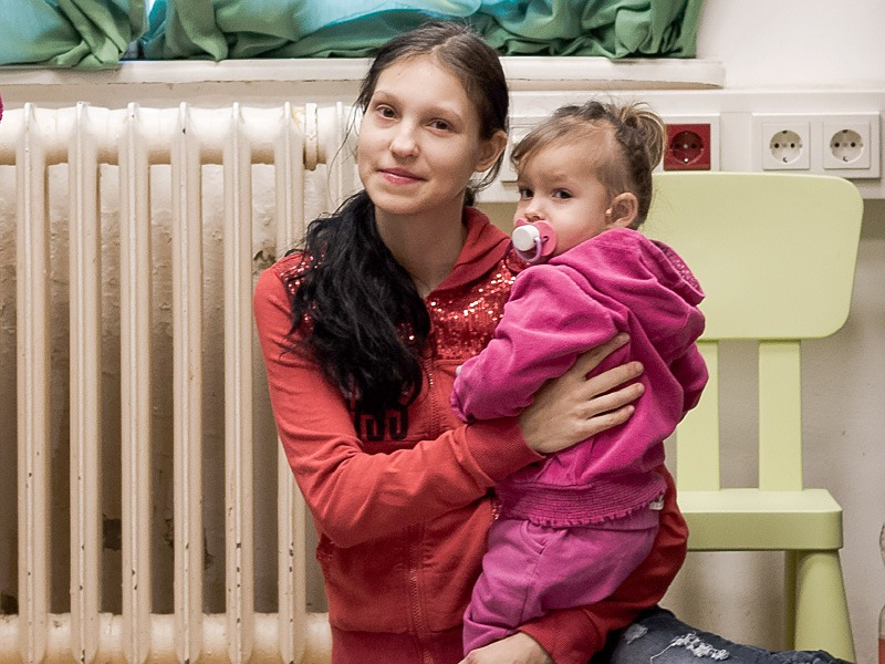 Eine Frau hält ihre kleine Tochter im Arm und sitzen vor einem Heizkörper.