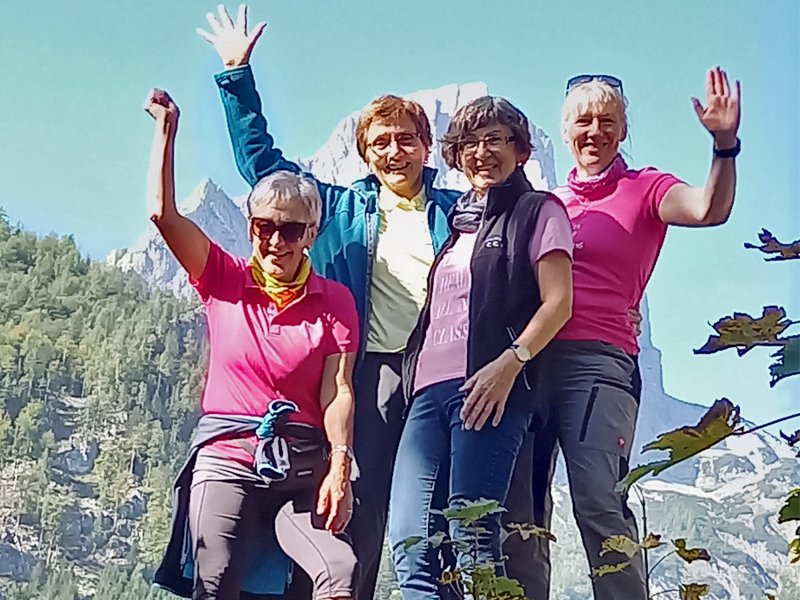 Vier Personen stehen in Wanderkleidung im Freien und winken.