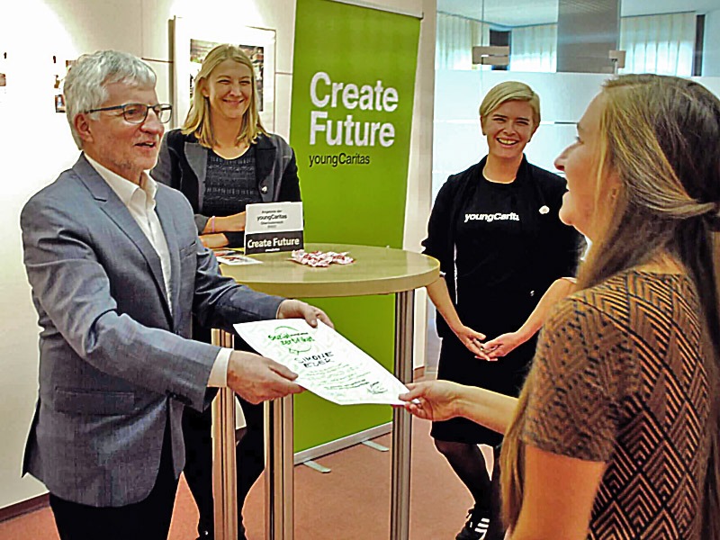 Der Caritas-Direktor überreicht eine Urkunde an eine junge Frau.