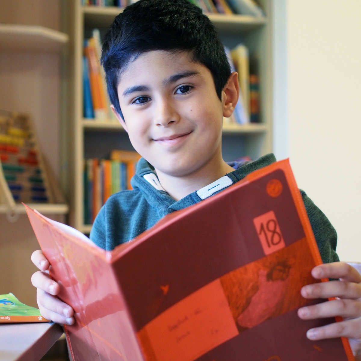Ein Junge hat ein aufgeschlagenes Schulheft in den Händen.