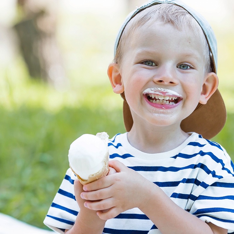 Ein Junge hält ein Eis in den Händen und grinst.