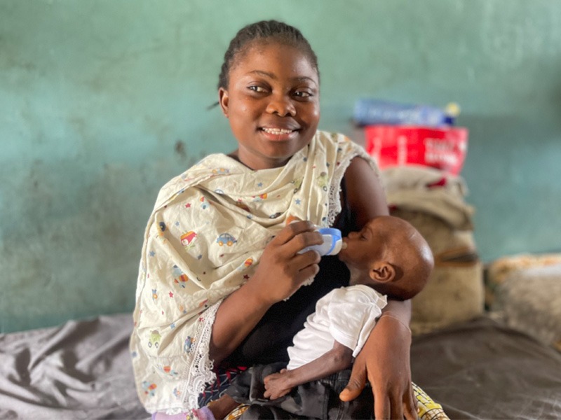Eine afrikanische Frau hält ihr abgemagertes Baby im Arm und füttert es mit einer Flasche.